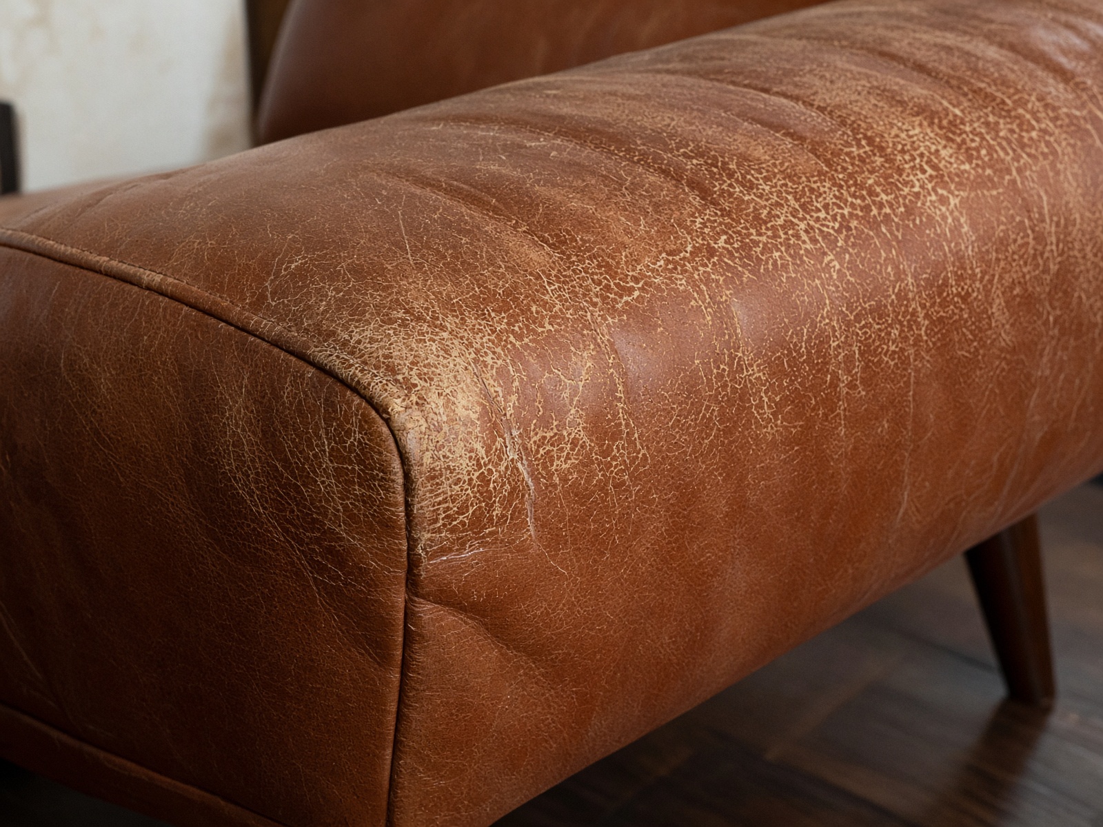 Close-up of worn cognac leather on a sofa arm that needs repair